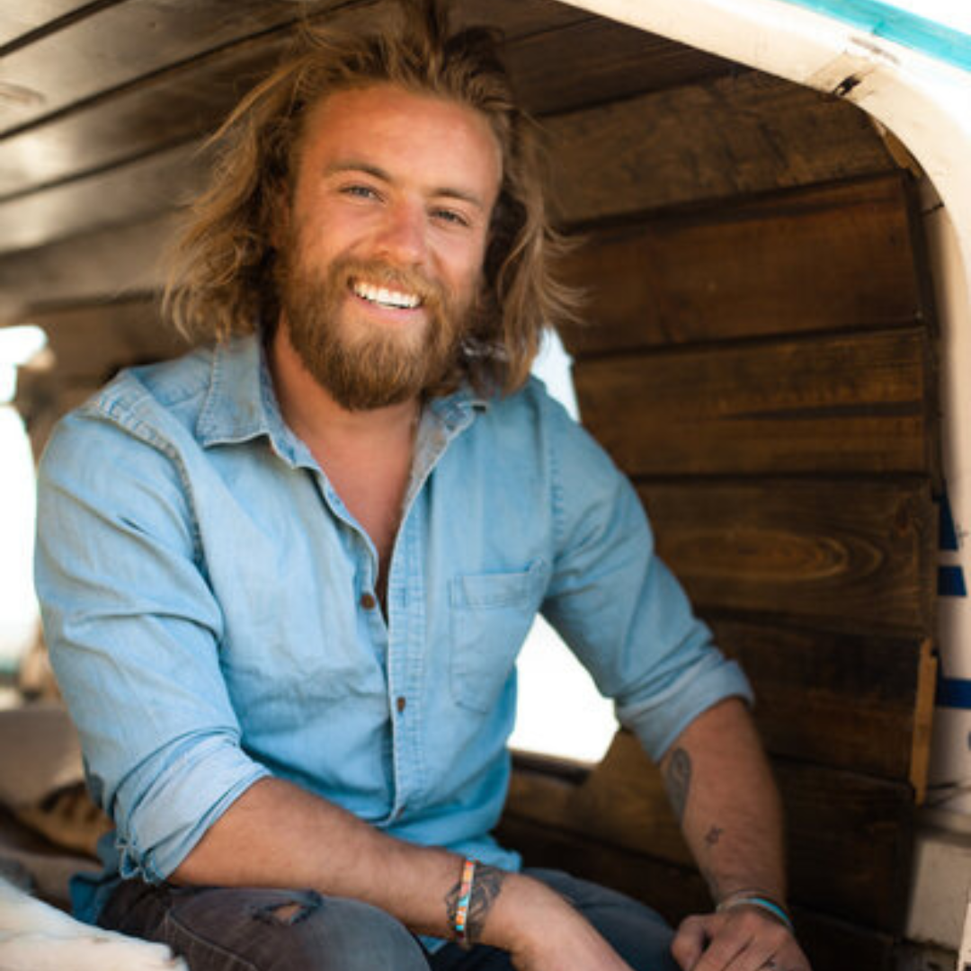Smiling man in a light blue shirt sitting inside a wooden structure