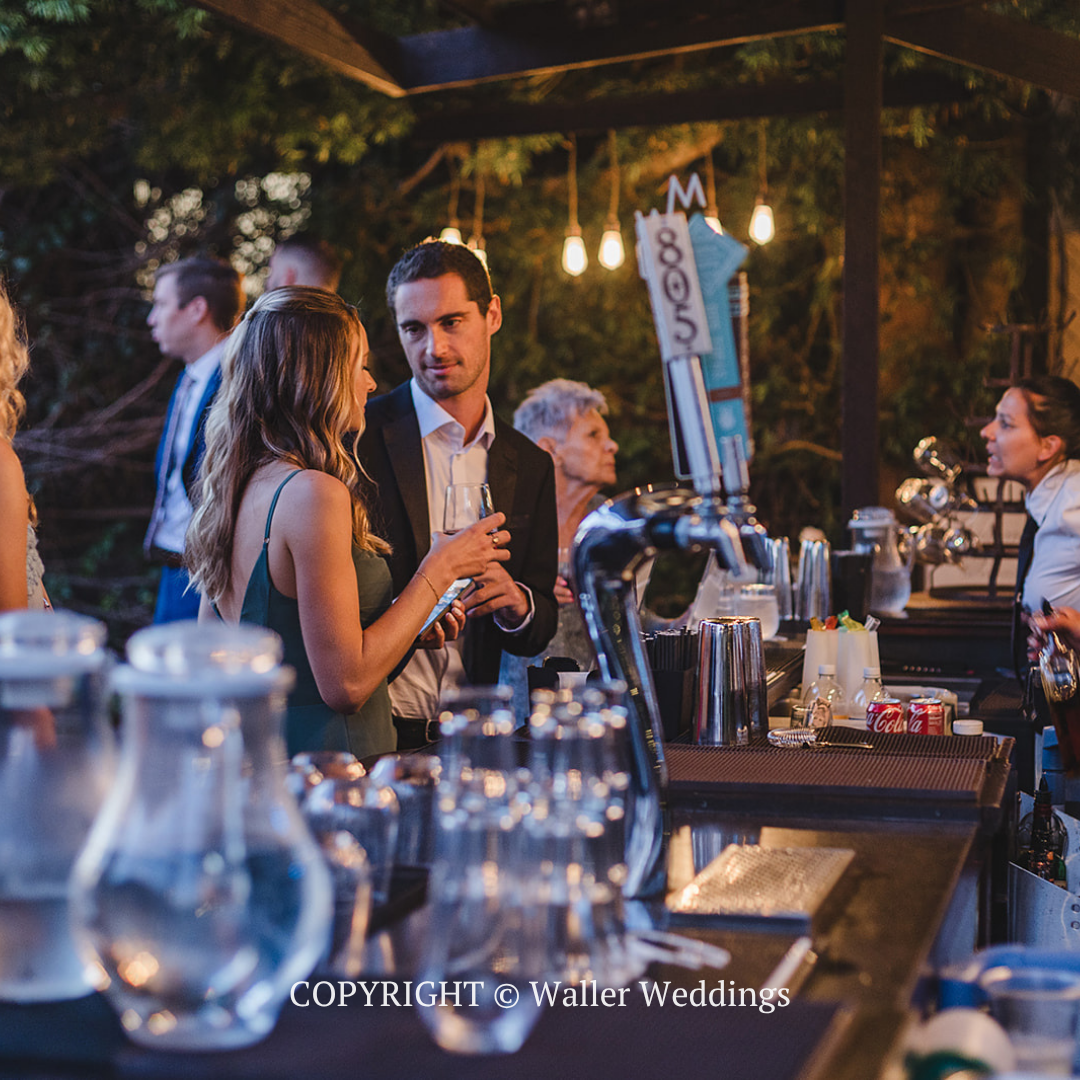 Guests mingling at an outdoor evening reception with drinks and warm string lights