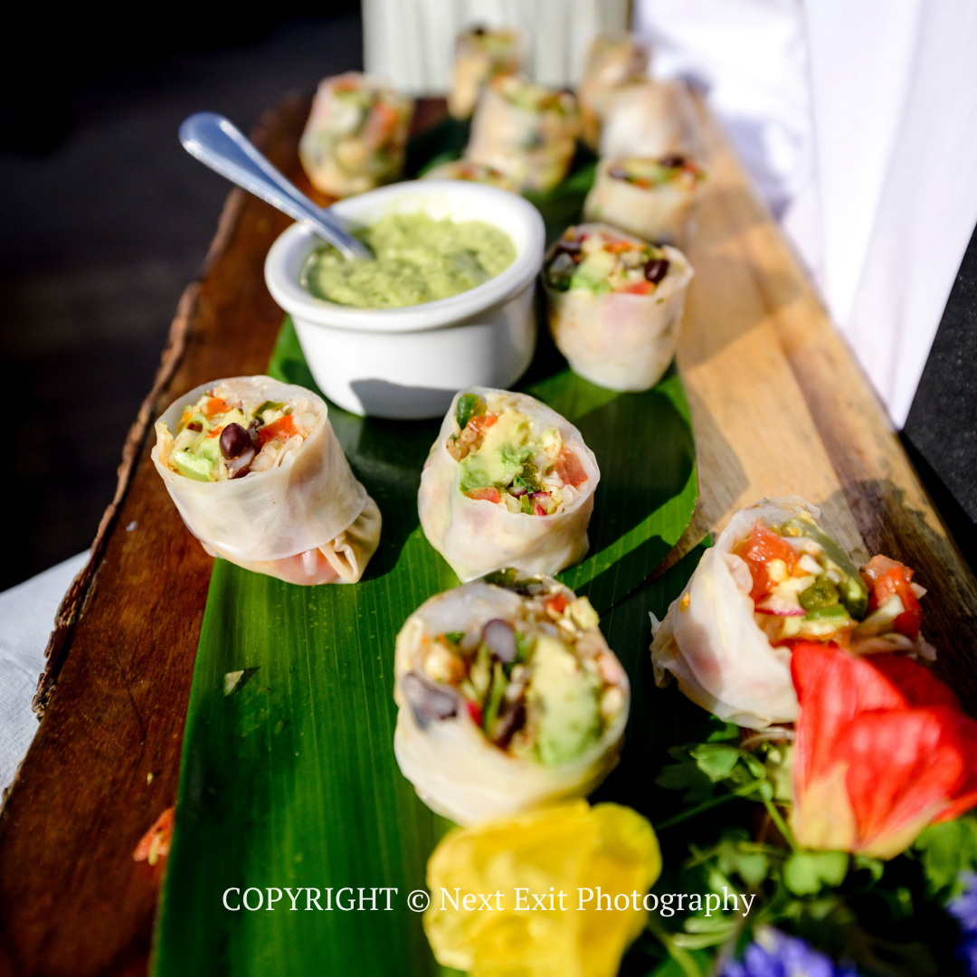 Vegetable spring rolls on a banana leaf with a bowl of green dipping sauce