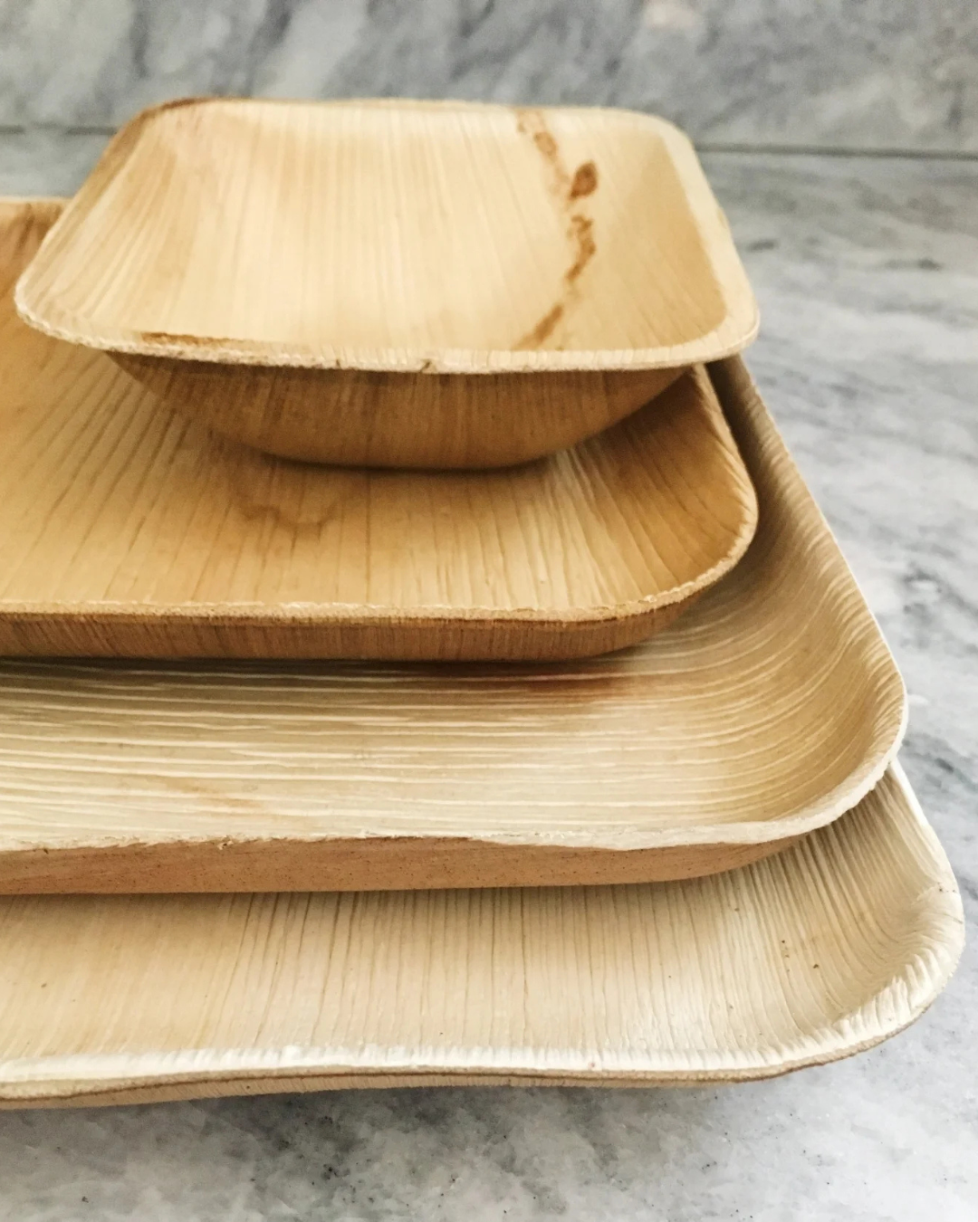 Stacked brown bamboo trays on a gray surface, with a small square bowl on top.