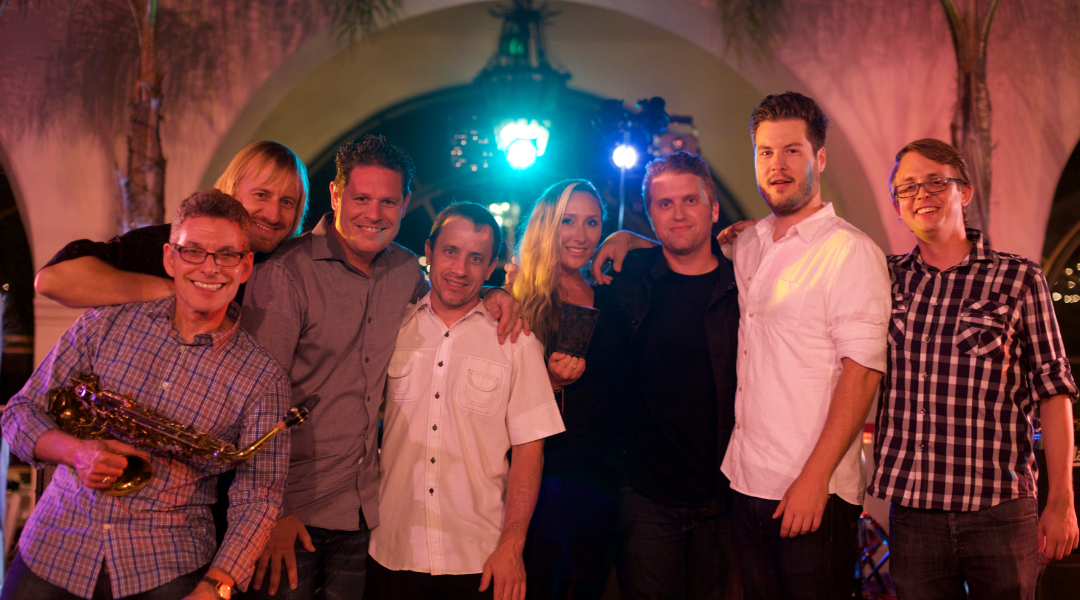 Group posing together under pink lighting at a party, with one person holding a bouquet.