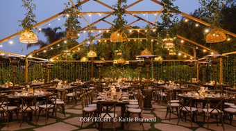Elegant outdoor dining venue with string lights, wooden beams, and tables set amid lush greenery at dusk