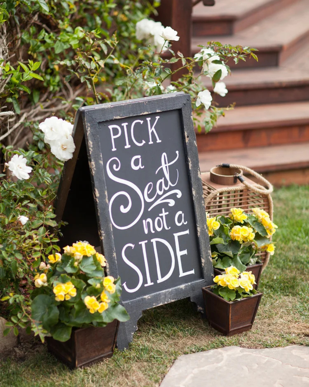 Chalkboard sign reading “Pick a seat, not a side” beside yellow flowers outdoors