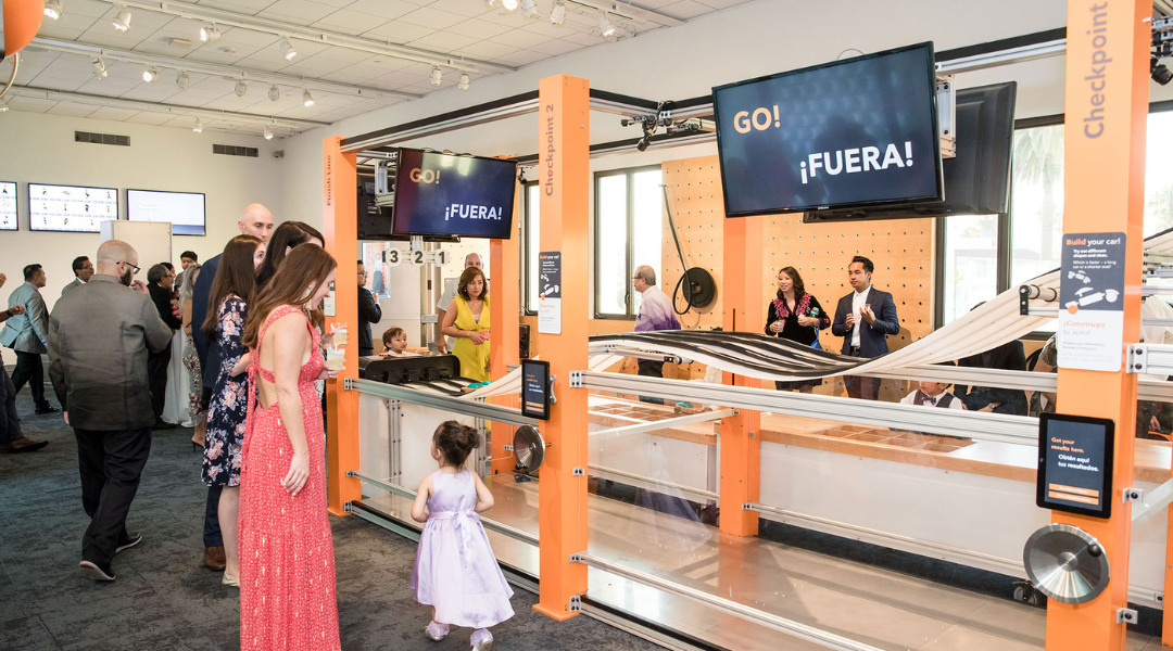 Airport check-in counter with travelers, orange signage, and a child in a pink dress waiting nearby