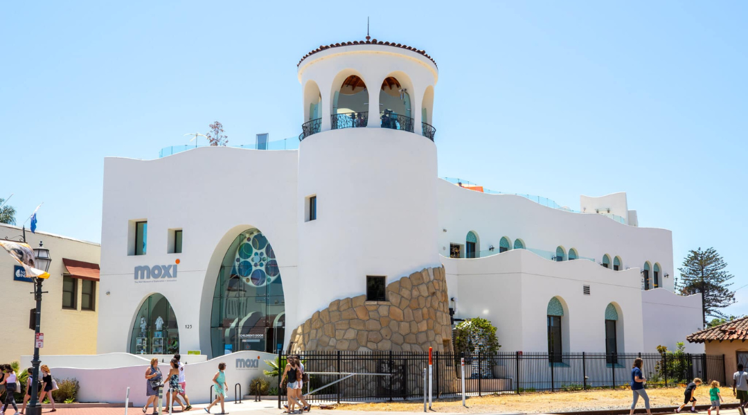 White stucco building with arched windows and a tower, under a clear blue sky
