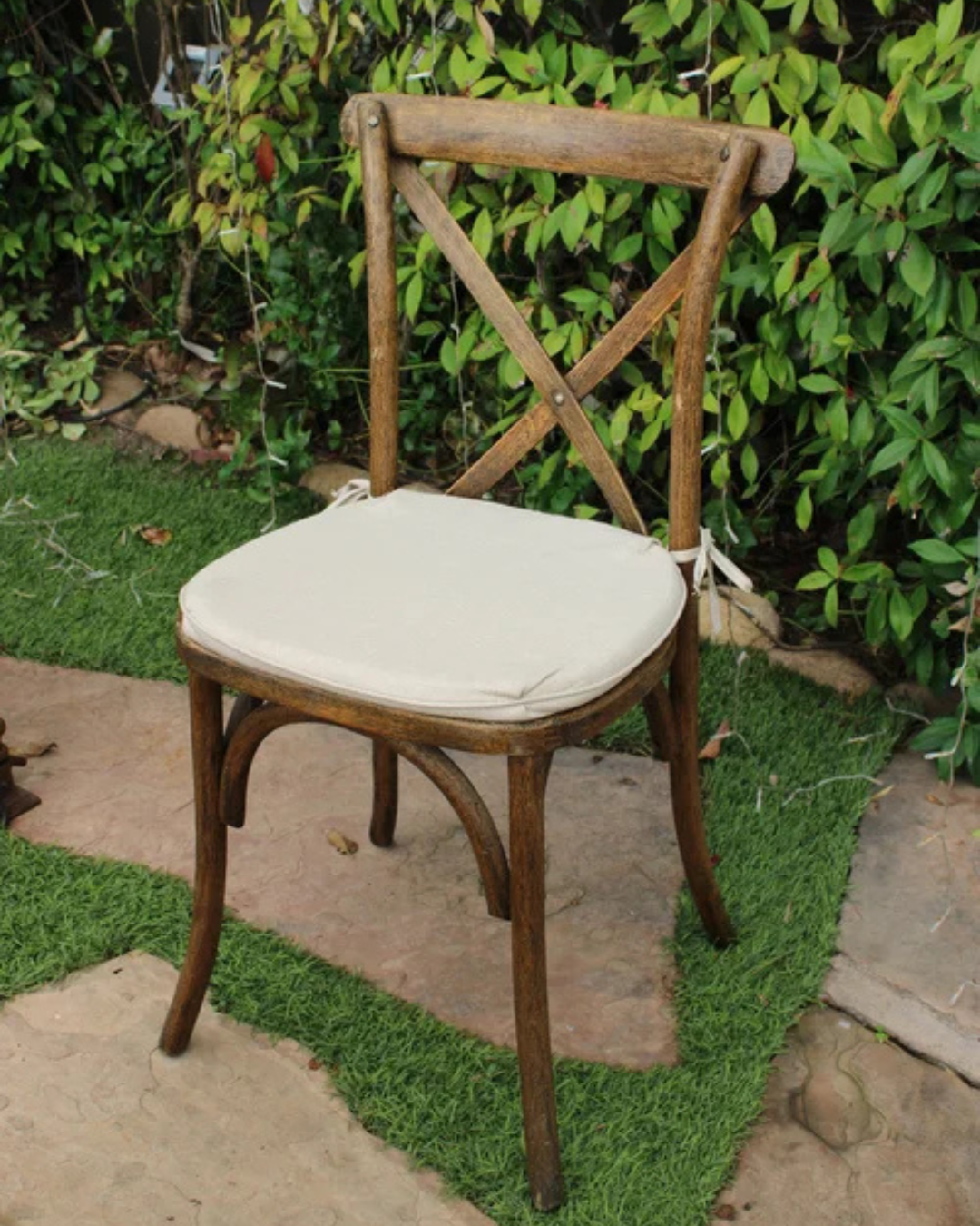 Wooden chair with cream cushion on a stone patio beside a leafy hedge