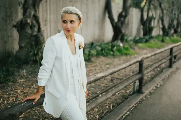 Person in white outfit leaning on a railing beside a tree-lined path