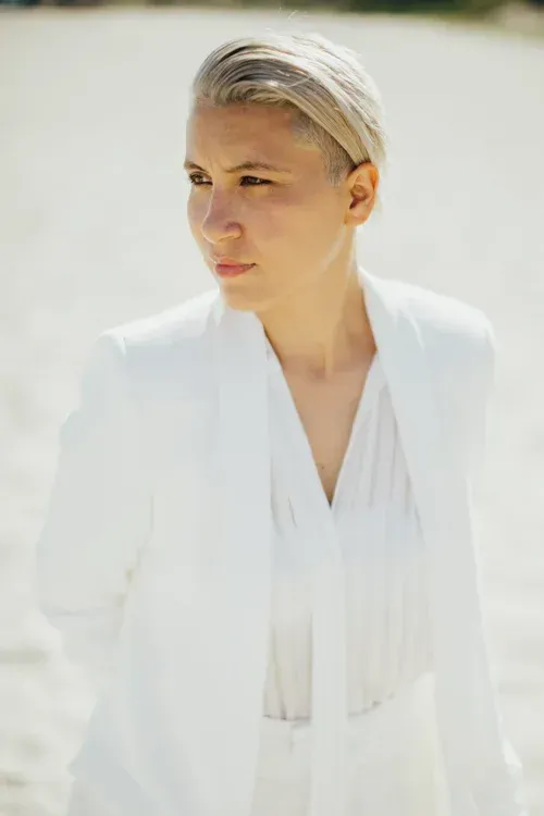 Person in a white suit standing outdoors in bright sunlight, looking to the side.