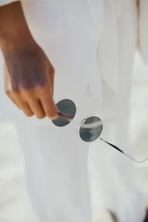 Hand holding round sunglasses over a white shirt with a thin black cord nearby
