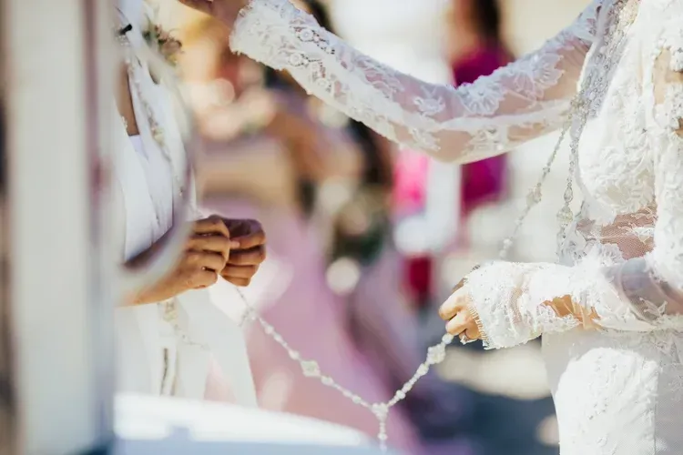 Hands holding a white wedding cord during a ceremony, with blurred guests in the background