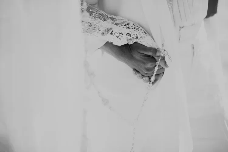 A hand holding white lace fabric, with sheer white curtains in the background