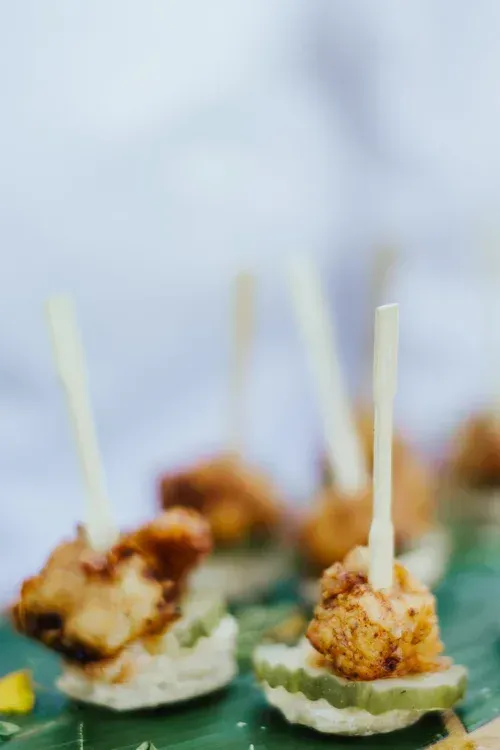 Mini appetizer bites on crackers with wooden picks, arranged on a green tray.