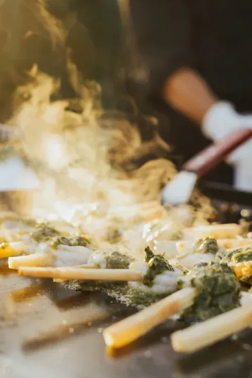 Stir-fried vegetables sizzling in a pan with steam rising and a spatula in the background