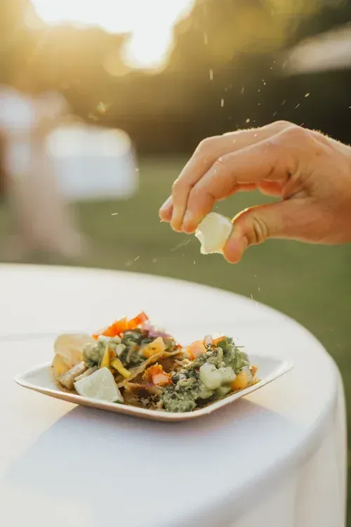 Hand sprinkling seasoning over a plated salad on an outdoor table at sunset