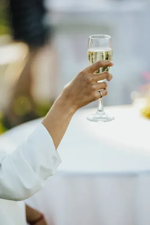 Person in white sleeve raising a champagne flute at an outdoor event