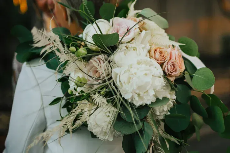 White and blush bridal bouquet with greenery held by a person in a white dress
