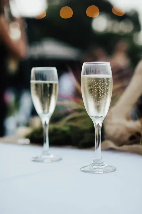 Two champagne flutes on a table at an outdoor event, one partially filled and one with bubbly prosecco.