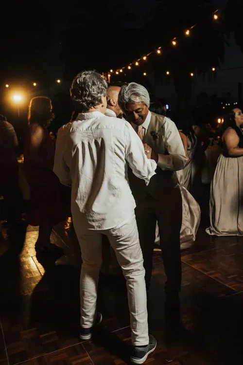 Two people dancing outdoors at night under string lights, surrounded by other guests.