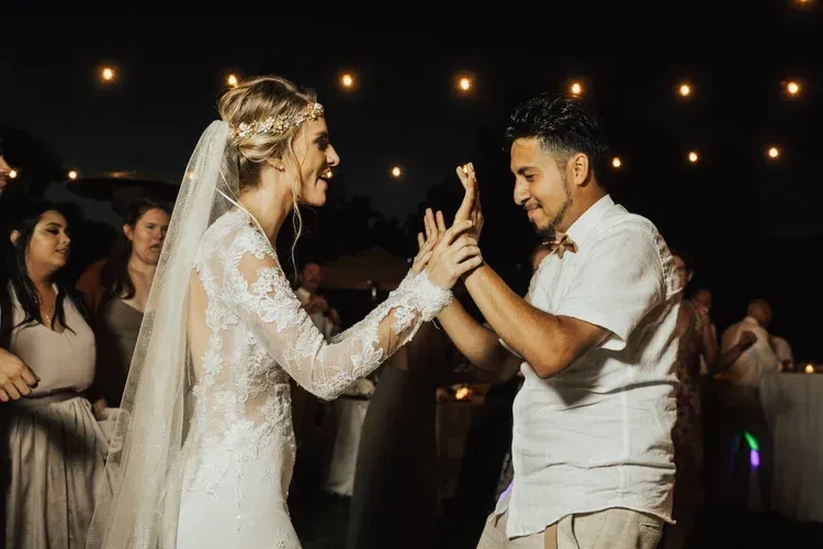 Bride and groom smiling during a lively wedding dance at night with warm string lights