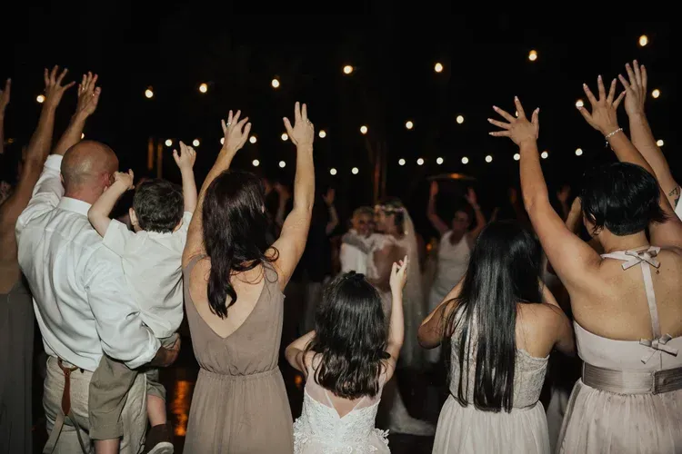 Guests with raised hands at an outdoor evening party under string lights