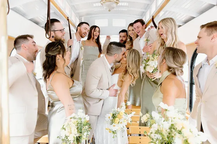 Wedding party in white outfits gathered in a bright hall, smiling and chatting during a celebration.