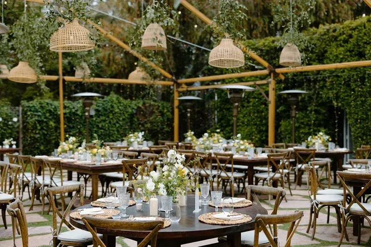 Outdoor garden wedding reception with round tables, white tablecloths, and hanging woven lanterns