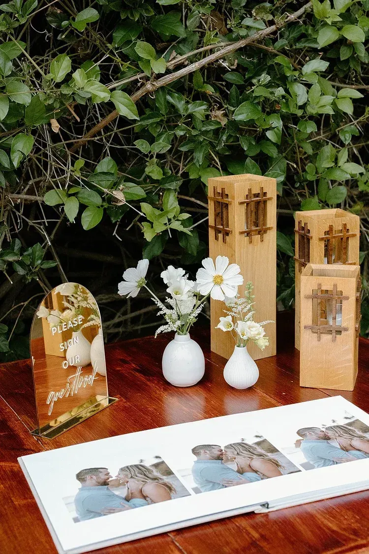 Wedding display with flowers, carved wooden plaques, and a photo album on a wooden table outdoors