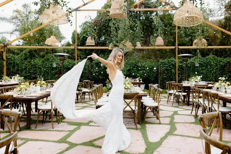 Bride in a white gown twirling in an outdoor garden reception with tables and hanging lights