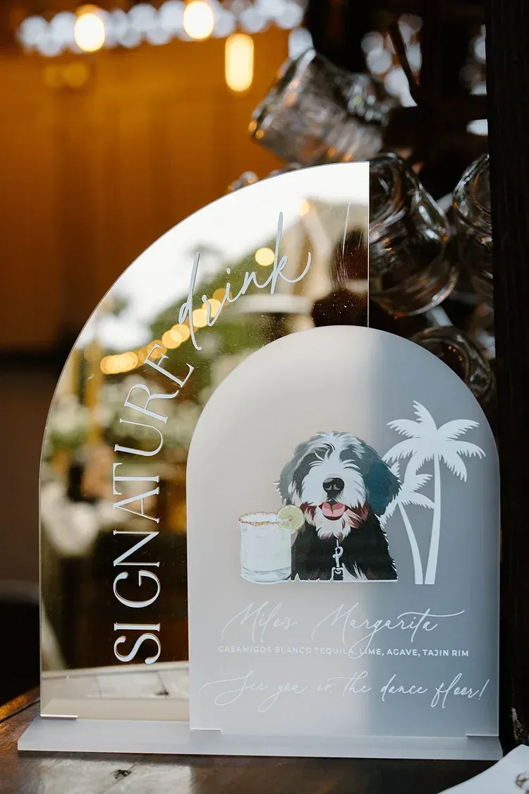Arch-shaped sign with a dog illustration, white palm tree graphic, and wedding-style text on a table