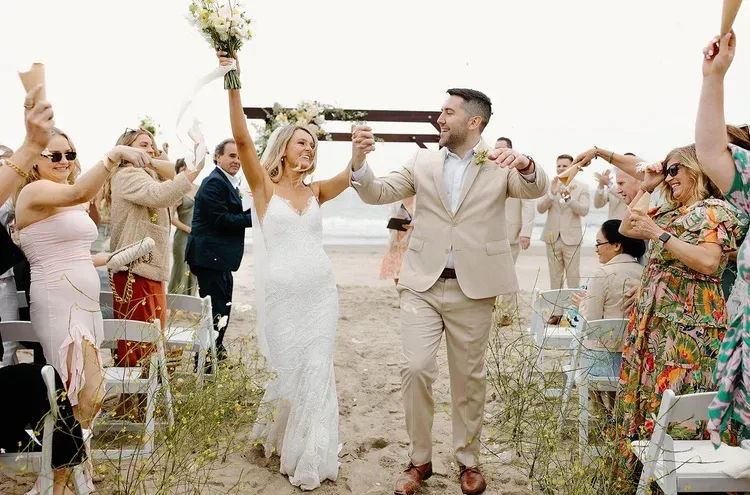 Wedding couple walking down aisle, smiling guests cheering and raising hands on both sides