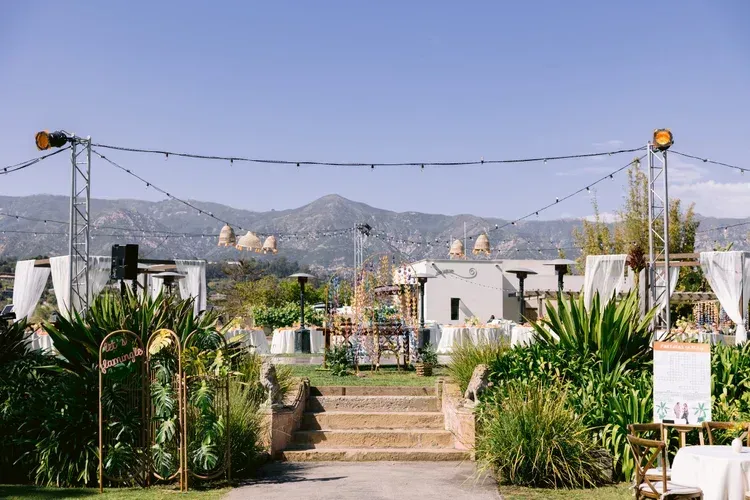 Garden path leading to white buildings with mountains in the background and string lights overhead
