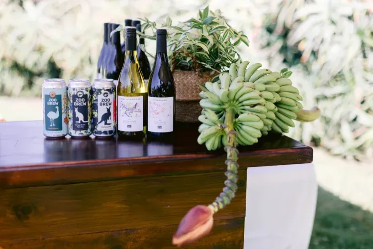 Wedding dessert table with wine bottles, canned drinks, and a hanging cluster of green bananas