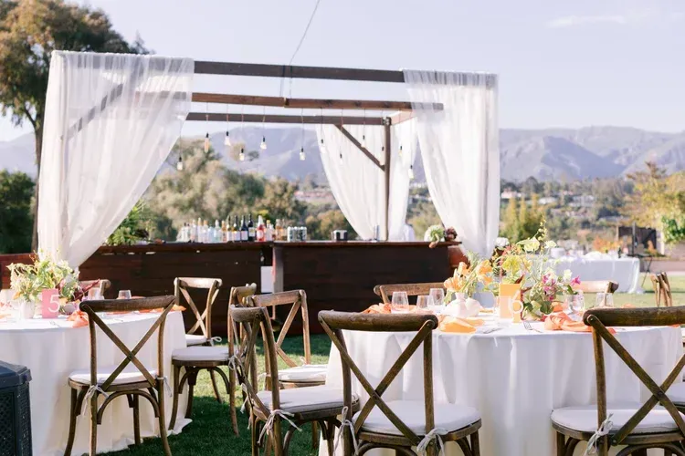 Outdoor wedding reception with white-draped tables, wooden chairs, and a scenic mountain view