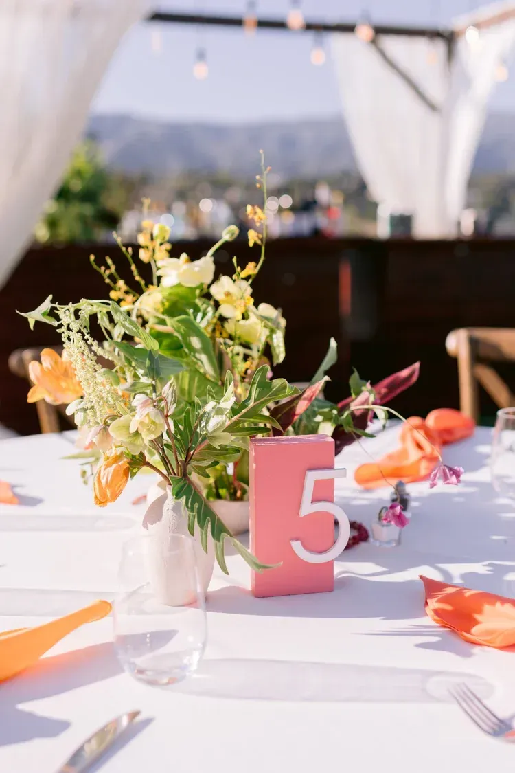 Outdoor wedding reception table with pink number 5 card and a floral centerpiece under a canopy