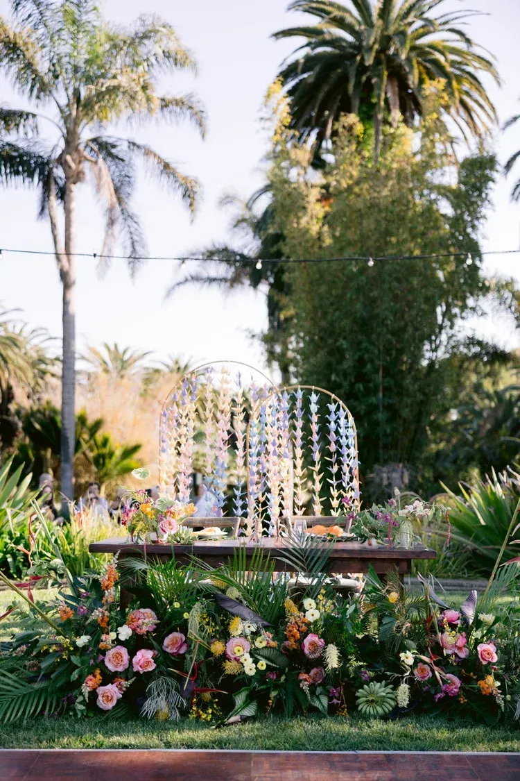 Flower-decorated fountain in a lush garden with tall palm trees and pink blooms