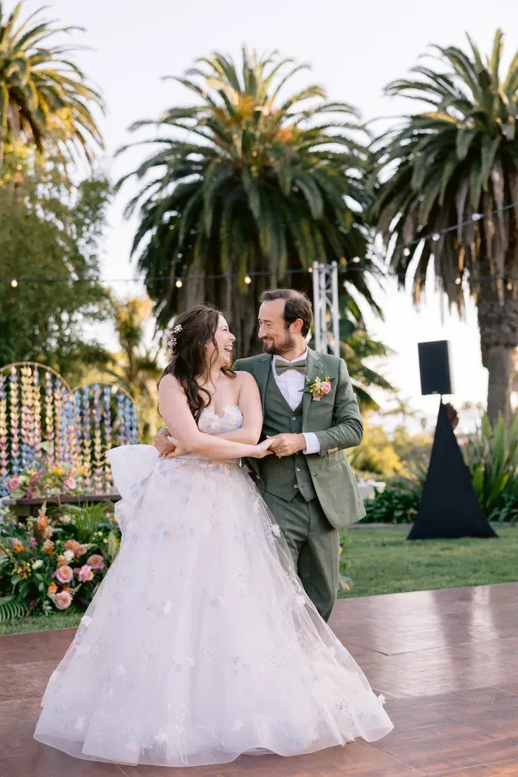 Wedding couple in white gown and green suit smiling in a garden with palm trees