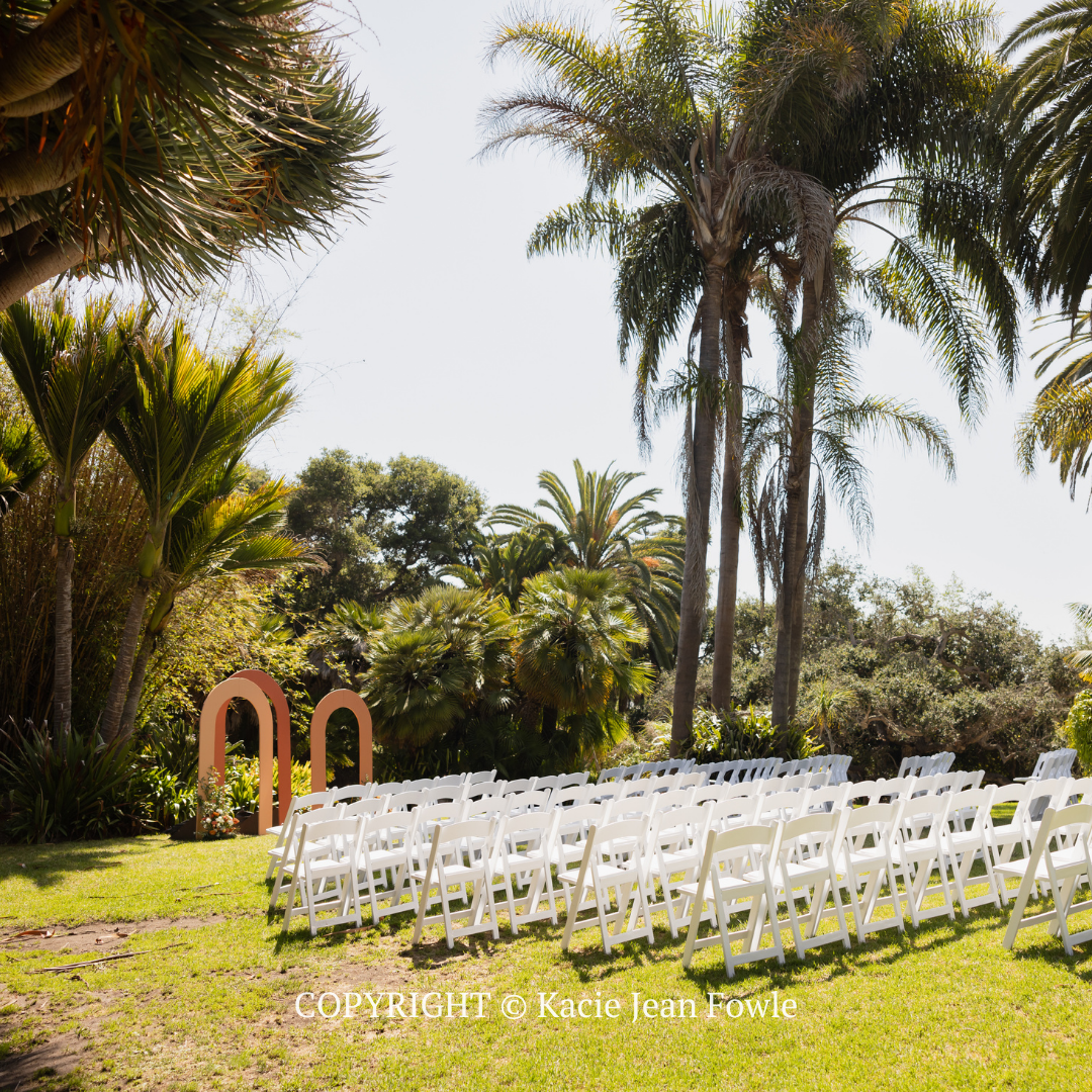 White chairs arranged on a grassy lawn in a tropical garden with palm trees, for an outdoor ceremony