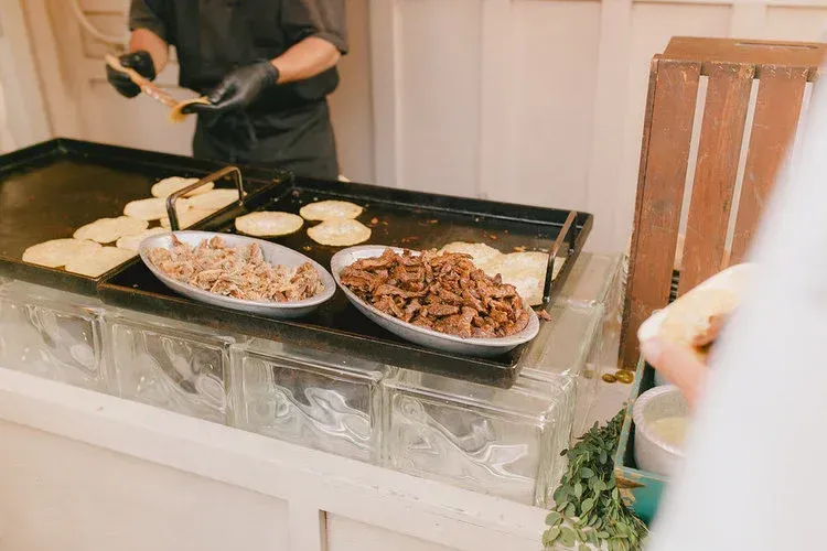 Tray of bagels and assorted toppings at a buffet station, with a person preparing them