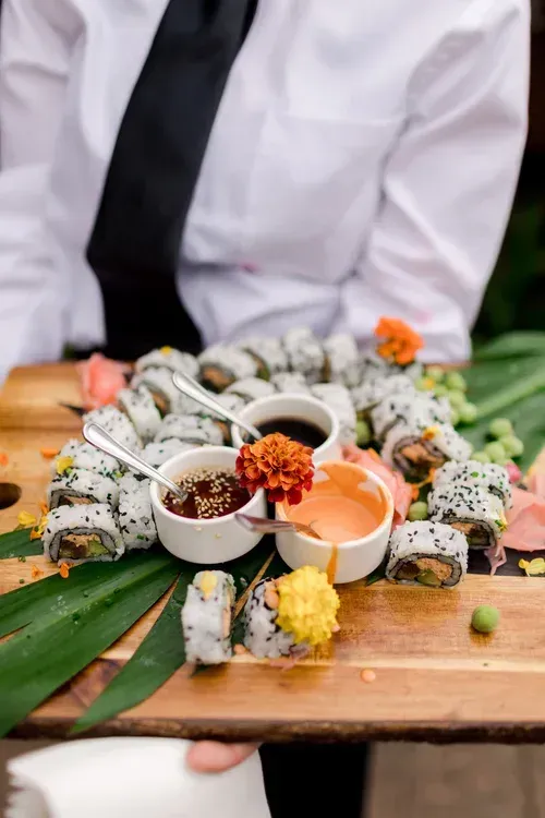 Sushi rolls and dipping sauces arranged on a wooden board, with a chef in a white jacket behind them