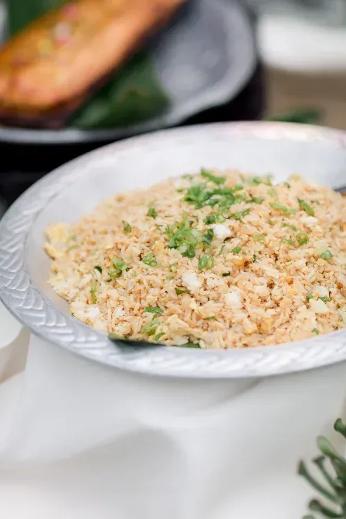 Plate of fried rice garnished with green herbs on a white table; blurred dish in background
