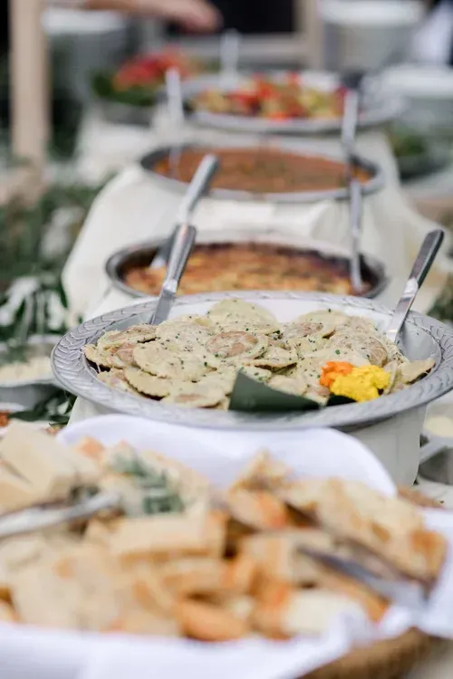 Buffet table with trays of assorted dishes, including sliced vegetables and appetizers, in a bright setting