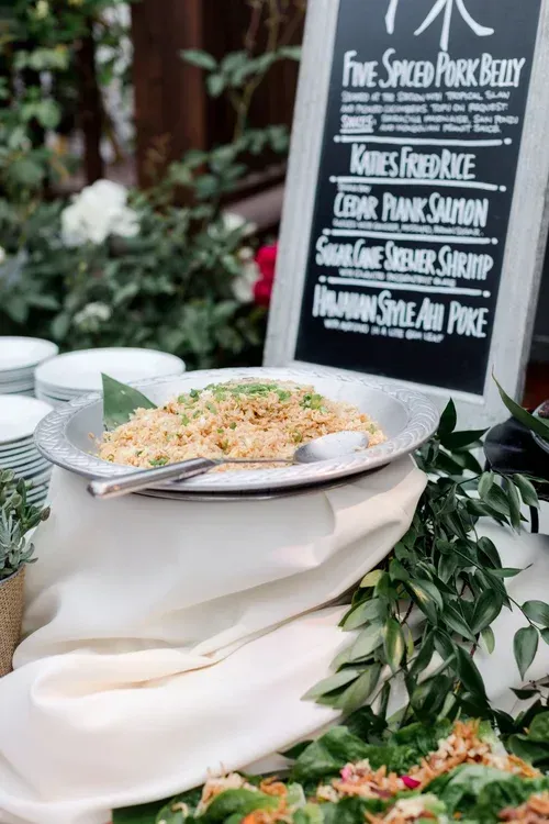 Buffet dish with herbs and grain beside a chalkboard menu at an outdoor event