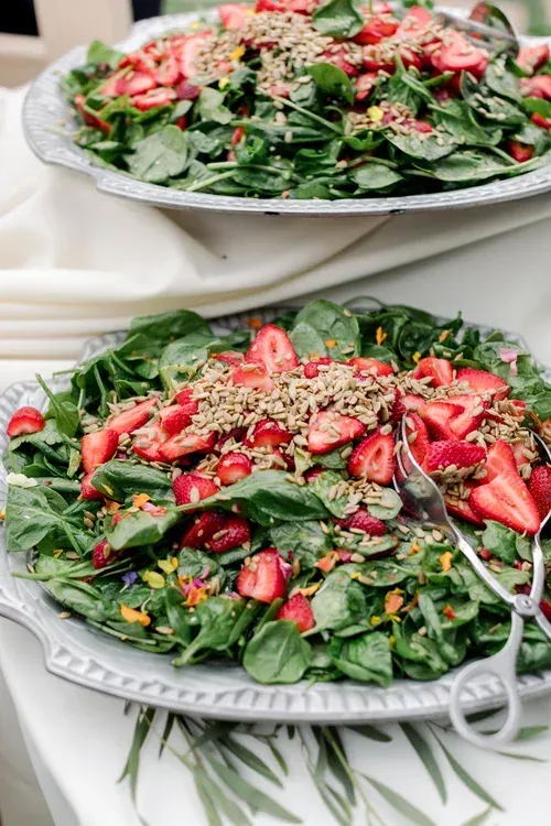 Two plates of leafy salad topped with strawberries and sesame seeds on a table