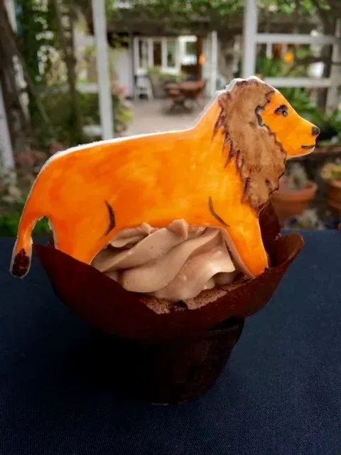 Orange lion figurine on a dark bowl with beige petals, outdoors with a blurred garden background