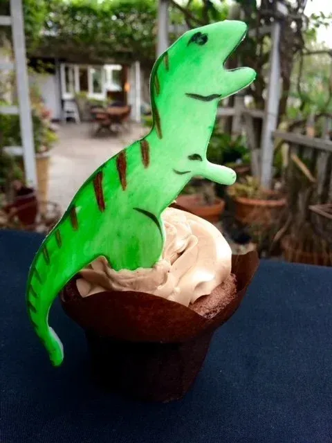 Green dinosaur-shaped topper on a chocolate dessert cup outdoors, with a blurred patio background
