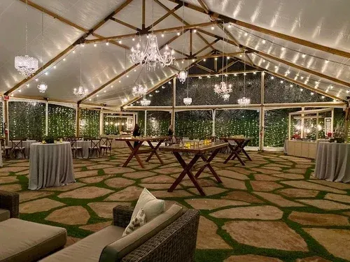 Elegant tented event space with string lights, chandeliers, and cocktail tables on a stone-patterned floor