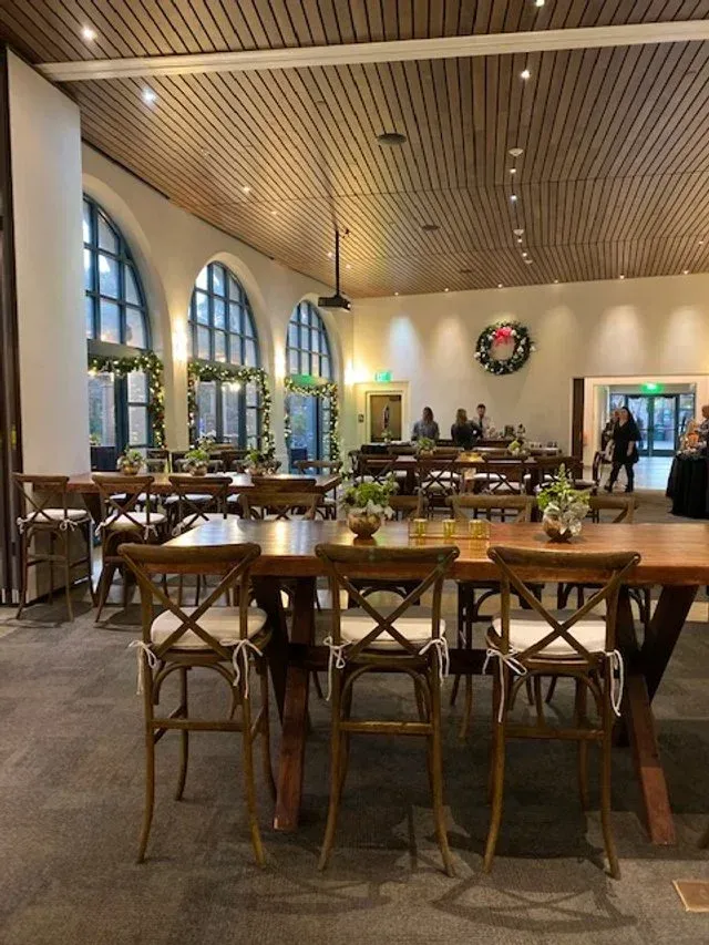 Spacious restaurant interior with wooden tables, arched windows, and a wreath on the back wall.