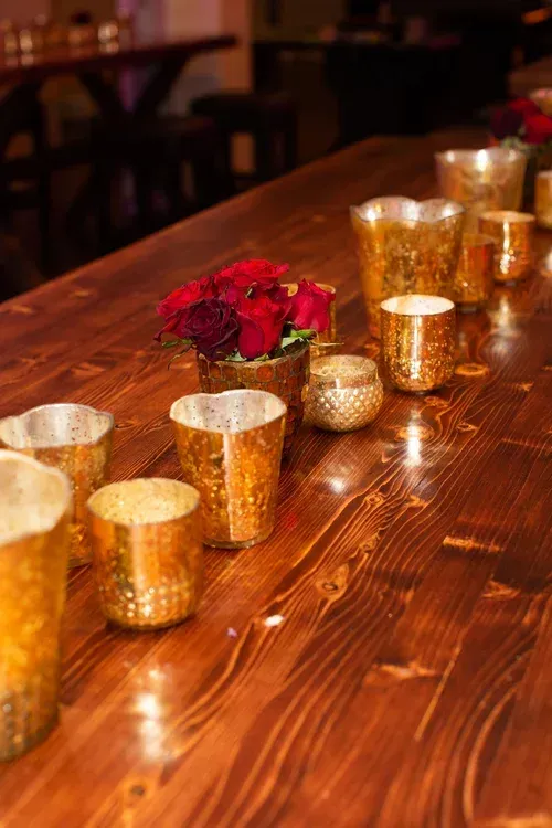 Small gold candle holders and red roses arranged on a wooden table in a dimly lit restaurant