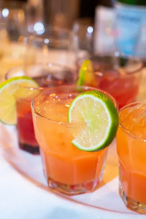 Colorful cocktails with lime slices on a table, likely at a party or bar.