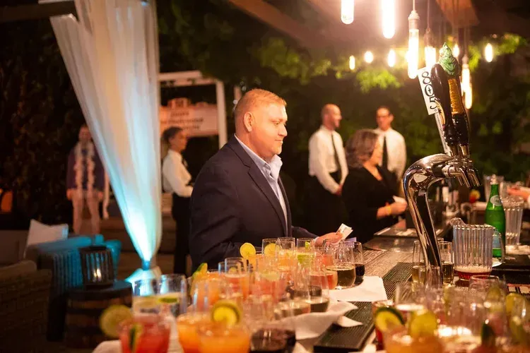 A man in a suit at a decorated dinner table, with drinks and candles in a warmly lit banquet hall.